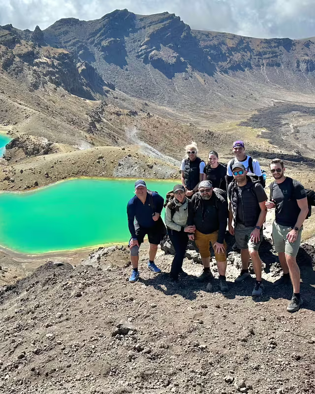 Skupina turistů během zájezdu na Novém Zélandu u smaragdových jezer Emerald Lakes v národním parku Tongariro. V pozadí vulkanická krajina s krátery.